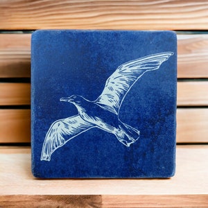 May include: A blue square tile with a white silhouette of a seagull in flight.