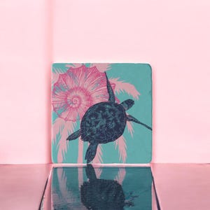 Peut inclure: Un dessous de verre carré bleu turquoise avec un motif floral rose et blanc et une tortue de mer noire nageant au centre.