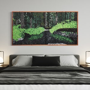 Puede incluir: Una obra de arte enmarcada que representa un mosaico verde y negro de una escena de bosque. La obra está colgada en una pared blanca sobre un marco de cama negro con ropa de cama gris.