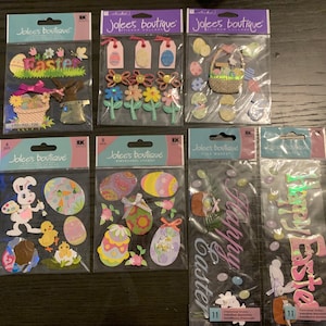 May include: A collection of Easter-themed dimensional stickers in various designs. The stickers include Easter eggs, bunnies, flowers, and baskets, with the word "Easter" featured on some packs. The stickers are packaged in clear plastic with colorful backing cards.