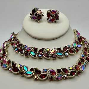 May include: A jewelry set consisting of a necklace and a pair of matching earrings. The pieces feature gold-tone metal settings adorned with marquise-cut deep red stones and iridescent, multi-colored cabochon stones arranged in a leaf pattern.