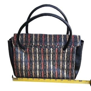 May include: A black leather handbag with a geometric patterned fabric flap. The fabric is black, white, orange, and brown. The bag has two black leather handles.