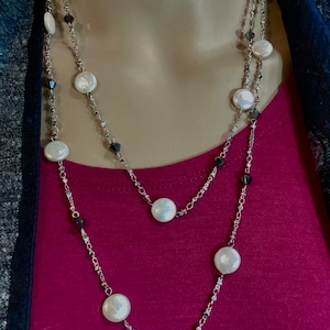 May include: A silver chain necklace with white pearl-like beads and black faceted beads. The necklace is layered and has a long length.