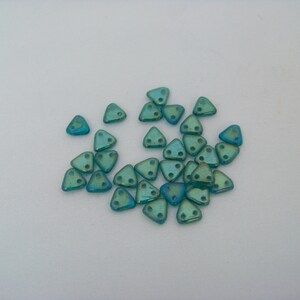 May include: A group of teal iridescent triangle shaped beads with two holes in each bead.