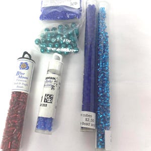 May include: An assortment of craft beads in various colors and shapes. Includes red seed and bugle beads, blue seed beads, teal pearl beads, and blue cube beads, all in clear tubes and bags. Ideal for jewelry making and crafting.