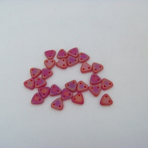 May include: A collection of small, triangular beads in shades of pink and orange. Each bead has three holes and a matte finish. The beads are scattered on a white surface.