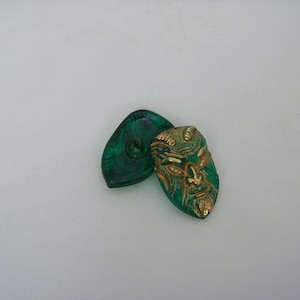 May include: Two green glass buttons, one with a gold-painted face design. The face has a beard and horns.