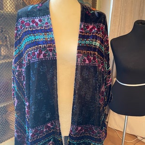 Puede incluir: Un kimono de terciopelo negro con un estampado floral y geom&eacute;trico colorido. El kimono tiene una silueta larga y fluida y es perfecto para superponer sobre un atuendo sencillo.