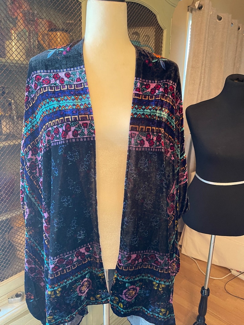 Puede incluir: Un kimono de terciopelo negro con un estampado floral y geom&eacute;trico colorido. El kimono tiene una silueta larga y fluida y es perfecto para superponer sobre un atuendo sencillo.