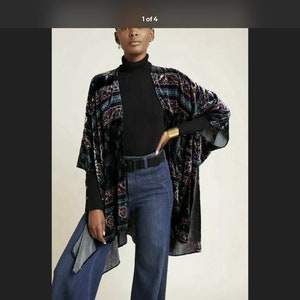 Puede incluir: Un kimono de terciopelo negro con un estampado geom&eacute;trico colorido. El kimono tiene mangas largas y una silueta ancha y fluida. Se lleva sobre una camisa de cuello alto negra y unos vaqueros azules.