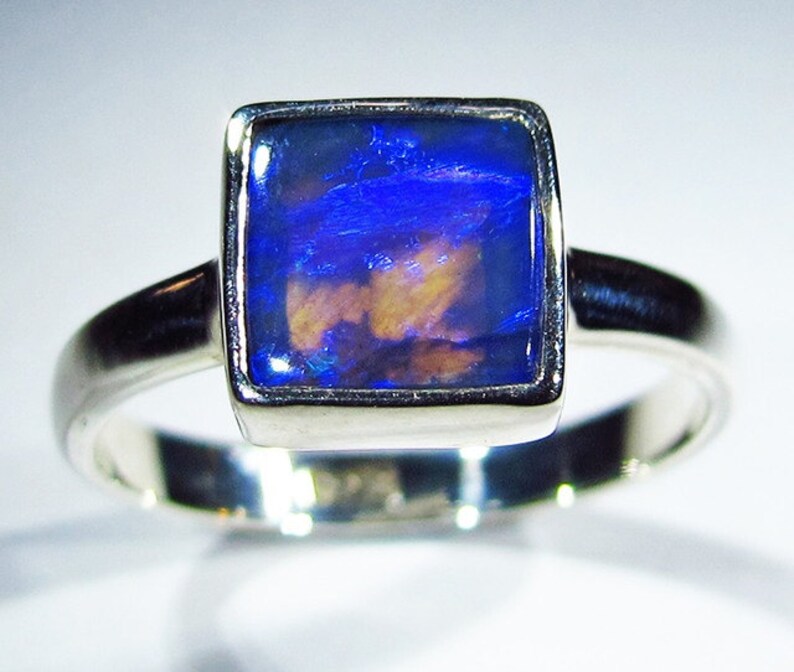 May include: A silver ring with a square blue opal gemstone set in a silver bezel.