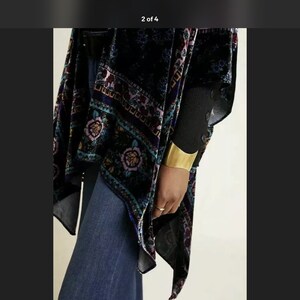 Puede incluir: Un kimono de terciopelo negro con un estampado floral colorido. El kimono tiene una silueta larga y fluida y es perfecto para superponer sobre un atuendo sencillo.