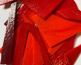 May include: A collection of red and orange glass pieces, some with a textured surface. The pieces are various shapes and sizes, and some have a slight curve.