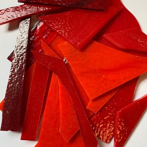 May include: A collection of red and orange glass pieces, some with a textured surface. The pieces are various shapes and sizes, and some have a slight curve.