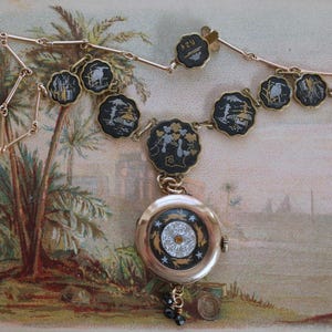Puede incluir: Un collar antiguo de tono dorado con un colgante redondo y varios elementos decorativos negros y dorados. El colgante presenta un dise&ntilde;o detallado con una gema central y un borde negro y dorado. El collar tiene una cadena delicada y peque&ntilde;os abalorios redondos.