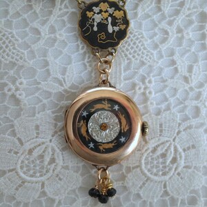 Puede incluir: Un collar con colgante dorado con un colgante redondo tipo reloj y una pieza superior circular m&aacute;s peque&ntilde;a. El colgante presenta un fondo negro con conejos y estrellas doradas, y un centro plateado y naranja. La pieza superior tiene un fondo negro con dise&ntilde;os florales dorados y blancos.