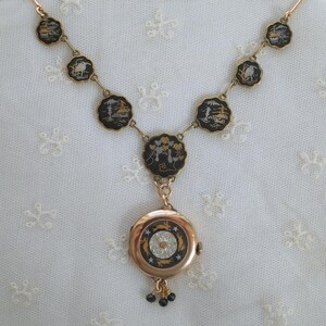 Puede incluir: Un collar dorado con colgantes circulares negros y dorados con dise&ntilde;os de paisajes. El collar tiene un colgante redondo con un dise&ntilde;o de esfera de reloj y peque&ntilde;os colgantes de cuentas negras.