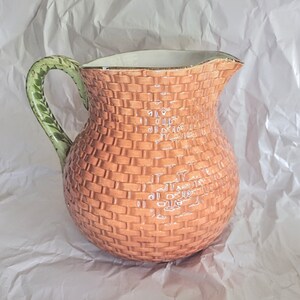 May include: A brown ceramic pitcher with a woven pattern and a green leaf-shaped handle.