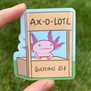 May include: A sticker featuring a cartoon axolotl with pink skin and blue eyes, sitting behind a wooden stand with the text "AX-O-LOTL" and "QUESTIONS 25£".