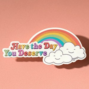 May include: A sticker with a rainbow and two clouds with smiley faces. The text "Have the Day You Deserve" is written in a retro font.