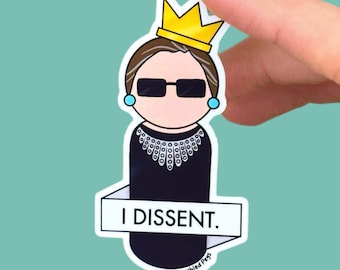 May include: A die-cut sticker featuring a stylized illustration of a figure wearing a yellow crown, black sunglasses, blue earrings, and a black garment with a white lace collar. A white banner across the front displays the text I DISSENT.