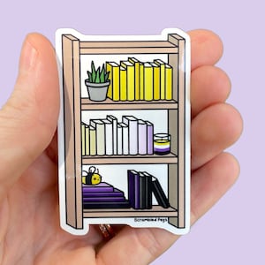 Puede incluir: Una pegatina de una estantería con tres estantes. El estante superior tiene una planta en maceta y libros amarillos. El estante del medio tiene libros blancos y morados. El estante inferior tiene libros negros, una abeja y una vela con una raya amarilla, blanca y morada. La pegatina dice "Scrambled Pegs" en la parte inferior.