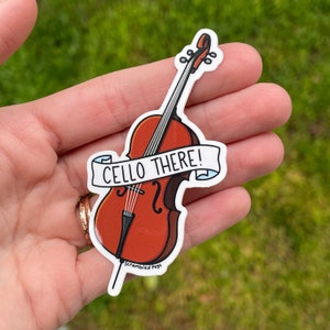 K&ouml;nnte beinhalten: Ein wei&szlig;er Aufkleber mit einer Cartoon-Illustration eines Cellos mit dem Text "Cello There!" und den Worten "Scrambled Pegs" unten.