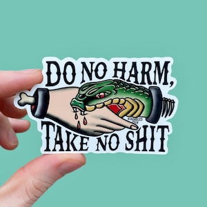 May include: A die-cut sticker featuring a green snake head emerging from a hand, with red blood drops and the black text DO NO HARM, TAKE NO SHIT. The design includes a bone-like end and a screw-like end, with the small text SCRAMBLED PEGS visible.