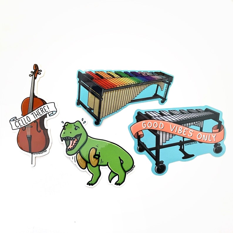 K&ouml;nnte beinhalten: Vier bunte Aufkleber mit einem Cello, einem Dinosaurier, einem Xylophon und einem Vibraphon. Der Cello-Aufkleber tr&auml;gt den Text "Cello There!" Der Dinosaurier-Aufkleber zeigt einen gr&uuml;nen Dinosaurier mit roter Zunge. Der Xylophon-Aufkleber zeigt ein Regenbogen-Xylophon mit einem Holzrahmen. Der Vibraphon-Aufkleber zeigt ein silbernes Vibraphon mit einem blauen Rahmen und dem Text "Good Vibes Only".