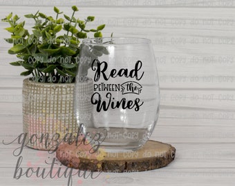 Könnte beinhalten: Ein klares, stieloses Weinglas mit dem Text "Read Between the Wines" in schwarzer Schrift. Das Glas steht auf einem Holzuntersetzer, mit einer kleinen Topfpflanze im Hintergrund. Der Topf ist hellgrau.