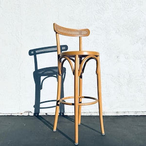 May include: A wooden bar stool with a woven cane back and seat. The stool has a round base and four legs.