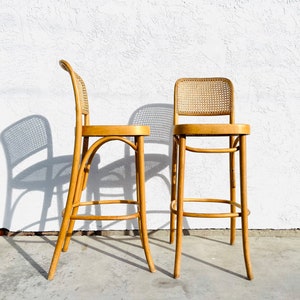 May include: Two wooden chairs with woven cane seats and backs. The chairs have a light wood finish and are in good condition.