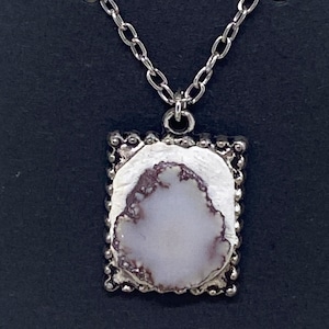 May include: A silver chain necklace with a pendant featuring a white and purple stone framed in a silver border.