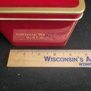 May include: Red tin box with a gold trim and the words "Johnnie Walker Red Label" printed on the side.