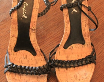 May include: A pair of black cork wedge sandals with braided straps and the word "Cupid" written on the insole.