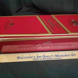 May include: Red metal tin with gold trim and the words "Johnnie Walker" and "Red Label" printed on the front. The tin is closed and has a gold hinge.