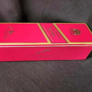 May include: A red and gold tin box with the words "Johnnie Walker" printed on the top. The box is closed and has a gold trim.