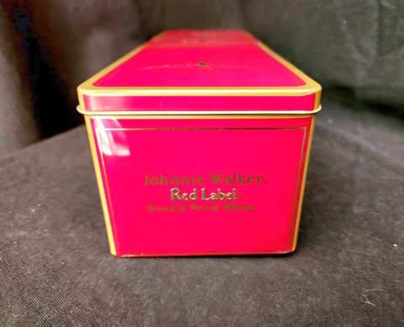 May include: A red and gold tin box with the words "Johnnie Walker Red Label Blended Scotch Whisky" printed on the front.