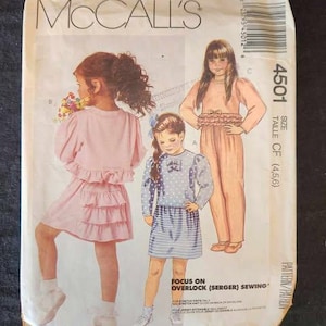 May include: Vintage McCall's sewing pattern featuring illustrations of children's clothing designs. The pattern includes drawings of a pink dress, a blue and white outfit, and a peach-colored jumpsuit. The pattern number is 4501.
