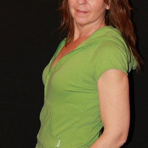 May include: A woman wearing a green short-sleeved shirt with a zipper and a black skirt.