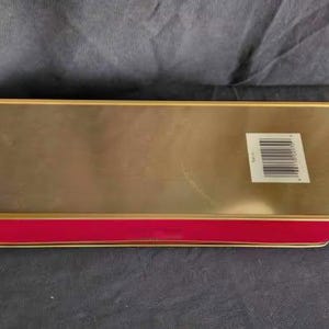 May include: A gold and red rectangular tin box with a barcode on the side.