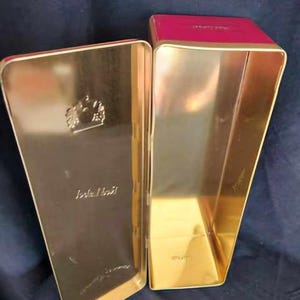 May include: An empty gold metal tin with a red lid. The tin has a crown design and the words "Johnnie Walker" printed on the front.