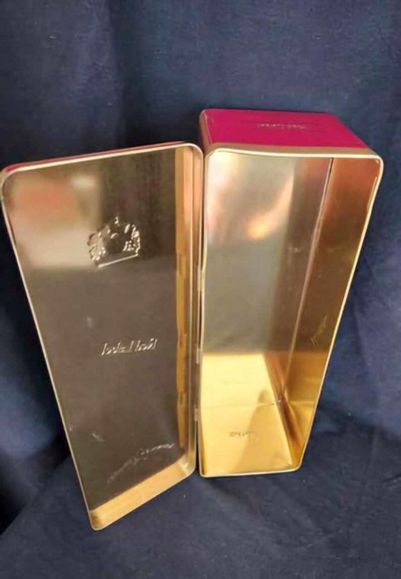 May include: An empty gold metal tin with a red lid. The tin has a crown design and the words "Johnnie Walker" printed on the front.