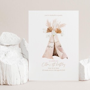 Puede incluir: Una tarjeta de invitación blanca con una ilustración de acuarela de un tipi, hierba de la Pampa y acentos florales. El texto dice "Estás invitado a una fiesta" y "5º cumpleaños de Chloe". La tarjeta se muestra sobre una superficie blanca texturizada.