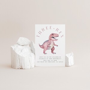 以下が含まれることがあります： ピンク色の恐竜のイラストと「THREE-REX」の文字が入った白い招待状。カードには「JOIN US AS WE CELEBRATE ISABELLA'S 3RD BIRTHDAY! MAY 1ST AT 2PM 123 MAIN ST CHICAGO, IL 12345」の文字も含まれています。
