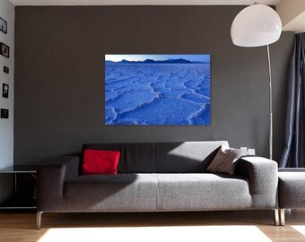 May include: A photograph of a blue, cracked, salt flat landscape. The salt flats are in the foreground, and a mountain range is in the background.