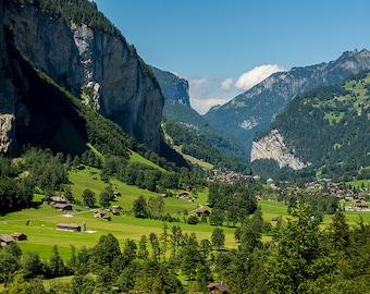 May include: A scenic view of a valley in the Swiss Alps. Lush green meadows and forests are surrounded by towering cliffs and snow-capped mountains. The valley is dotted with small houses and a village.