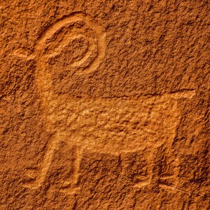 May include: A petroglyph of a bighorn sheep carved into a reddish-brown rock face.