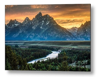 May include: A panoramic view of a mountain range with a river winding through a valley. The sky is a vibrant orange and yellow, creating a dramatic sunset over the peaks. The mountains are covered in snow and the valley is lush and green.