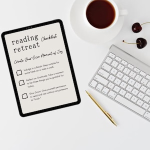 Pode incluir: Um tablet exibindo uma lista de verificação de retiro de leitura com o texto: reading retreat Checklist, Create Your Own Moment of Joy, Indulge in a Break, Reflect on Gratitude e Slow Down. Um teclado prateado, uma caneta dourada e duas cerejas.
